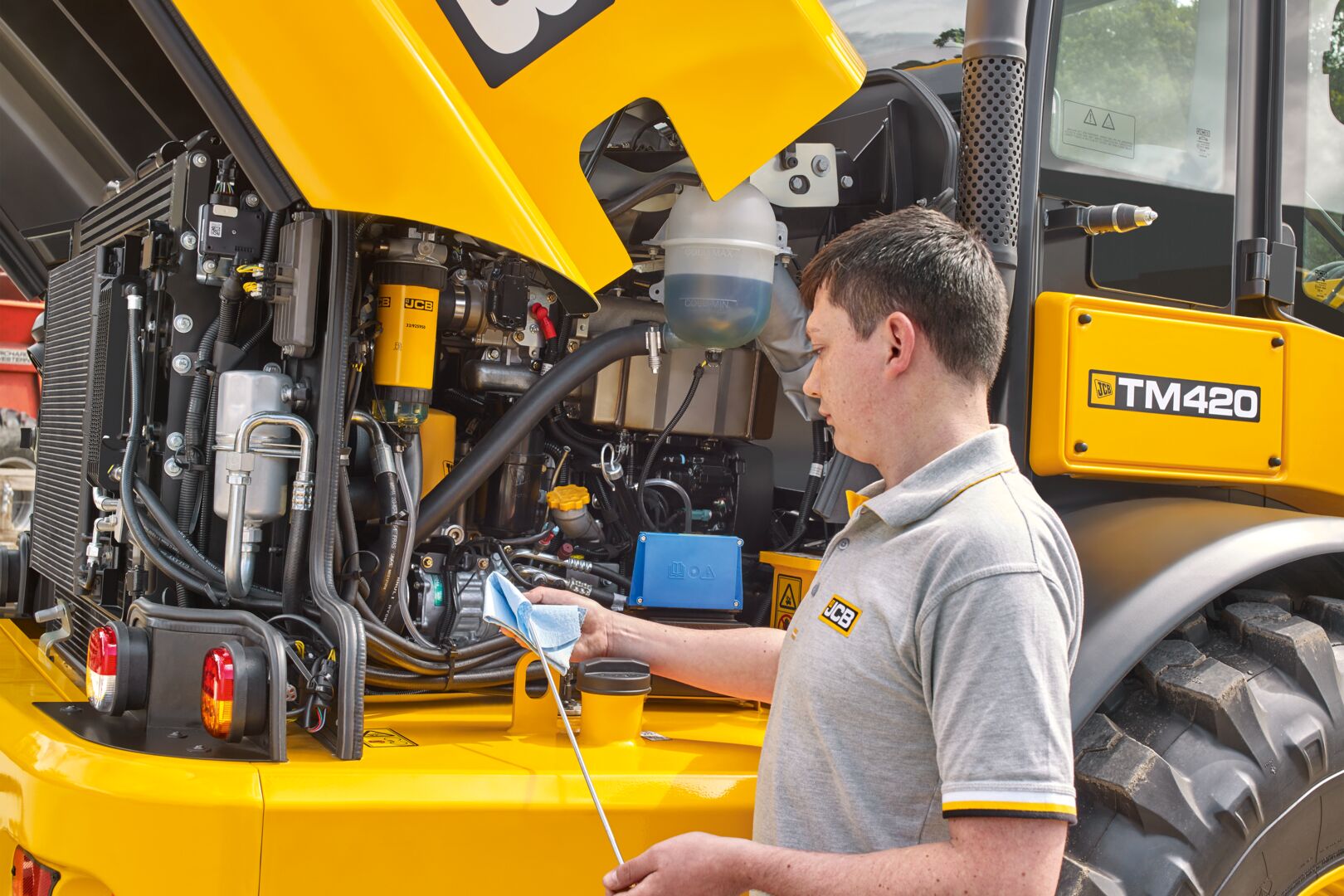 Technician inspecting the engine bay of a JCB TM420