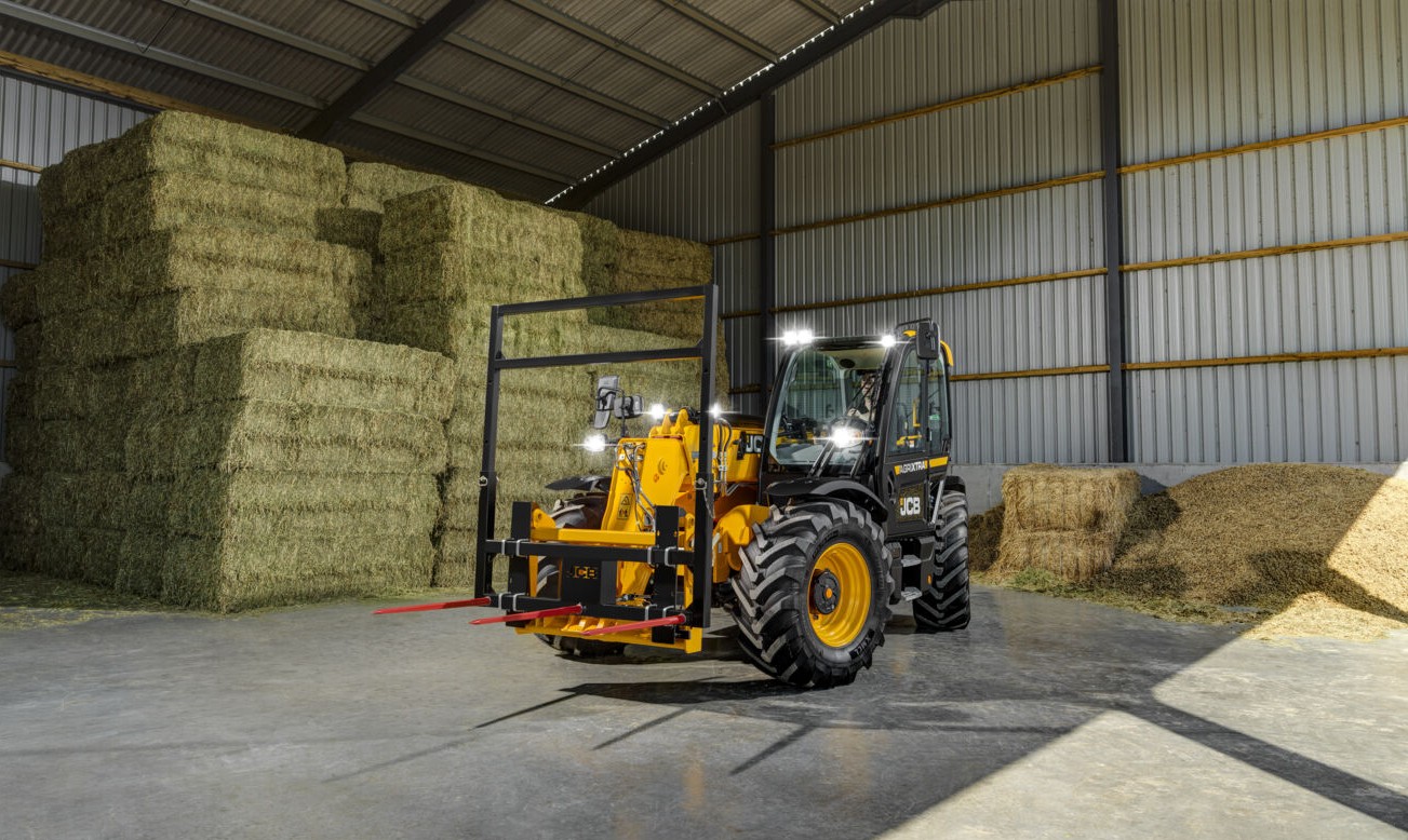 JCB telehandler with bale spike attachment moving hay bales inside a farm shed